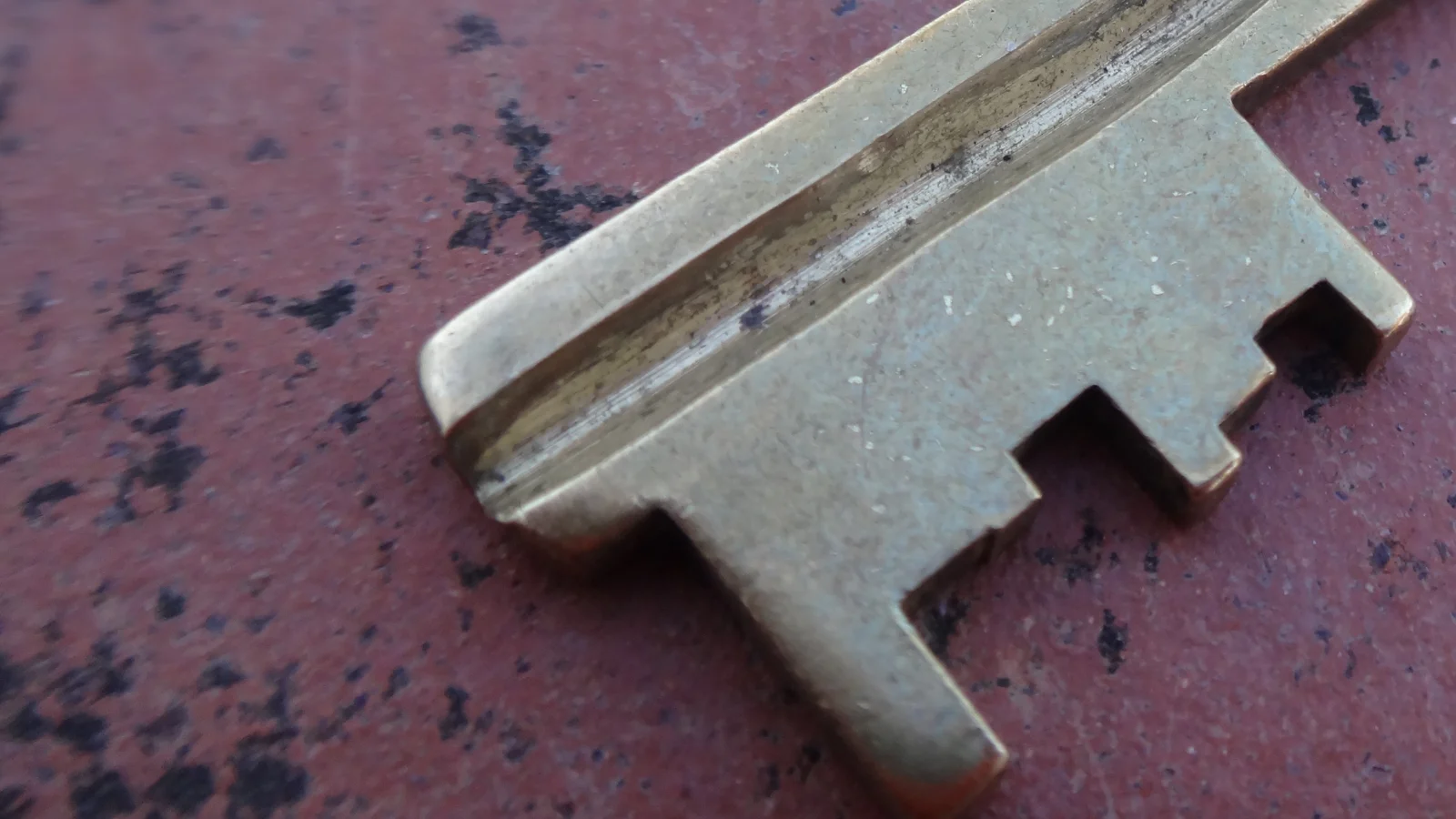Close-up of the blade and bit of an old brass key lying on a worn, dark red surface.